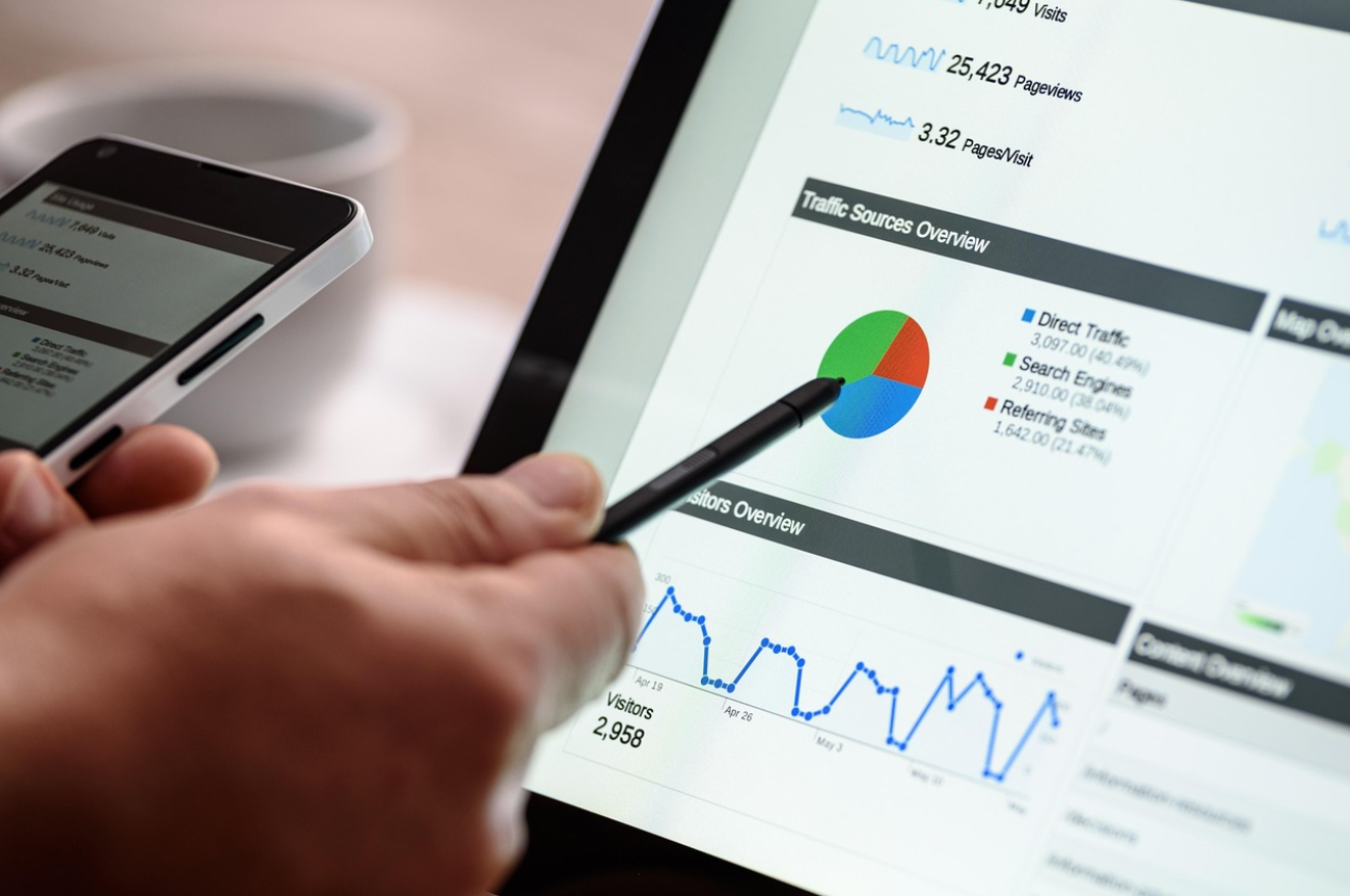 A person's hands holding a phone and a pen, pointing the pen at data on a screen.